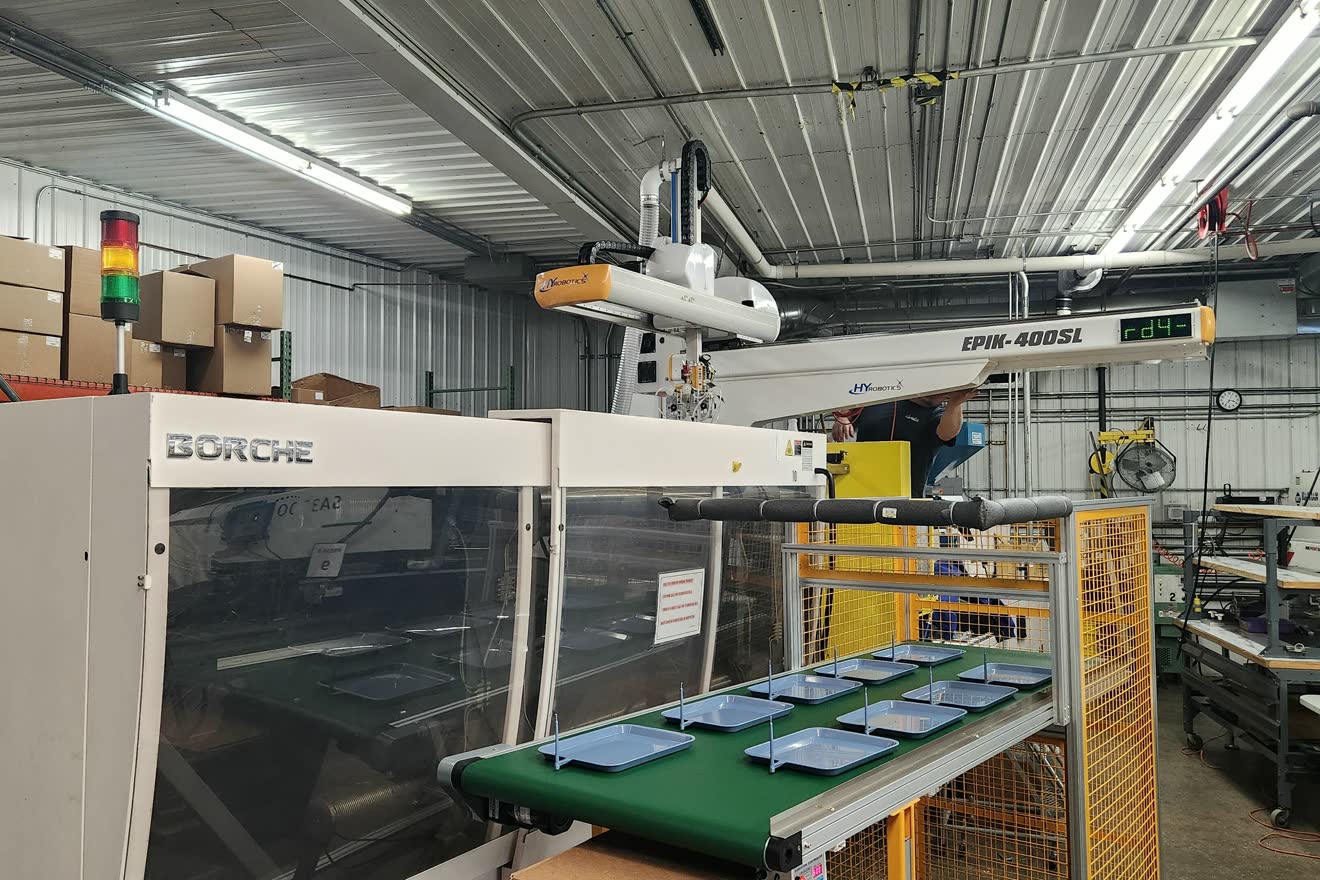 Moldeo por inyección de plástico: la máquina inyectora y el robot lineal que retira las piezas recién formadas sobre la banda transportadora